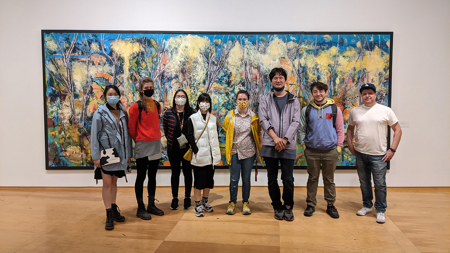 A group of students stand in front of a panoramic painting.