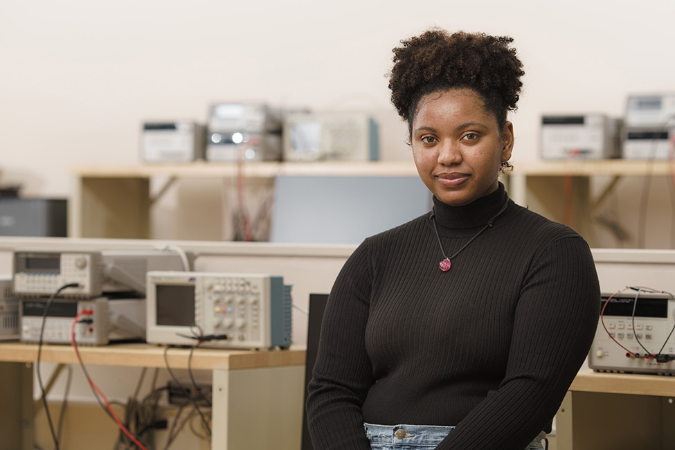 A RIT student engineer, Roxette Burgos, wearing a black turtleneck sweater and jeans in an electrical engineering lab.