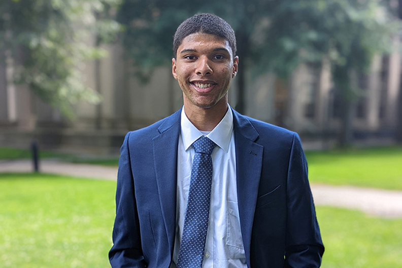 A headshot of RIT engineering student, Joseph Vazquez wearing a navy suit on MIT's campus.