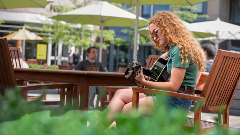 a photo of a student sitting outdoors playing guitar