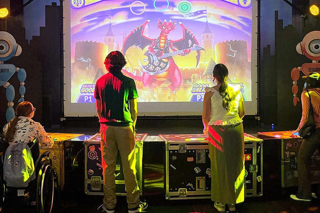 two women and two men stand in front of a video screen playing "Beat the Boss, an interactive game at The Strong National Museum of Play. 