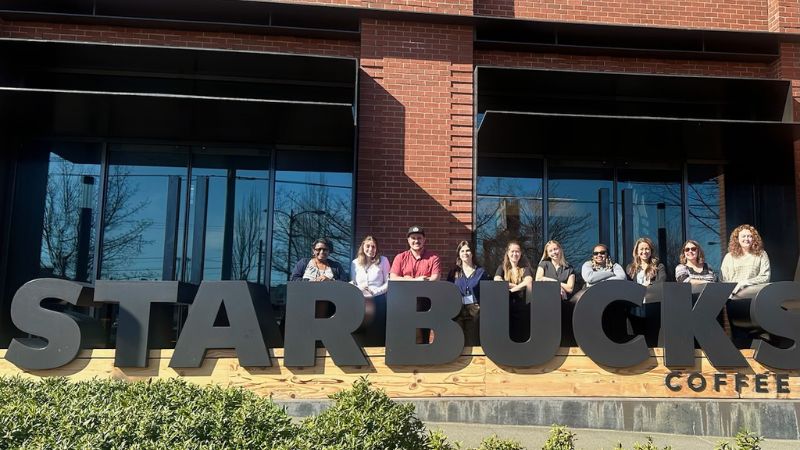 a group of honors students pose in front of the starbucks sign while on a trip to seattle