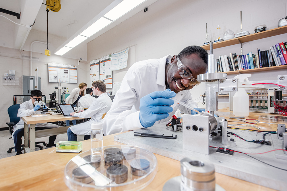 Davis Kipkania Kiboi wearing a lab coat and squeezing liquid out of a pipet onto a metal wheel.