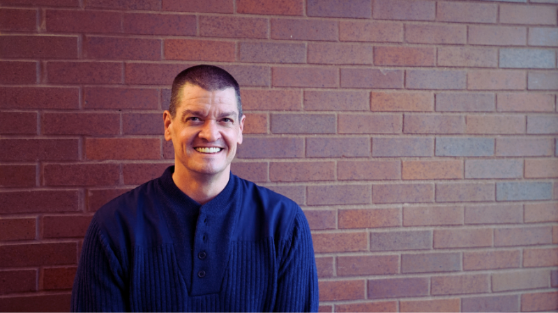 Chris Soukup posing for portrait in front of bricks.