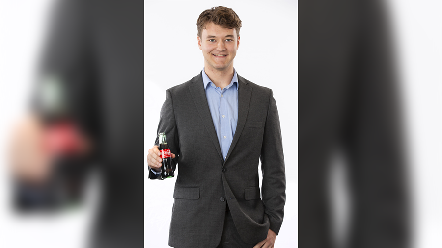 Jake O' Conner standing while smiling and holding a bottle of coca-cola