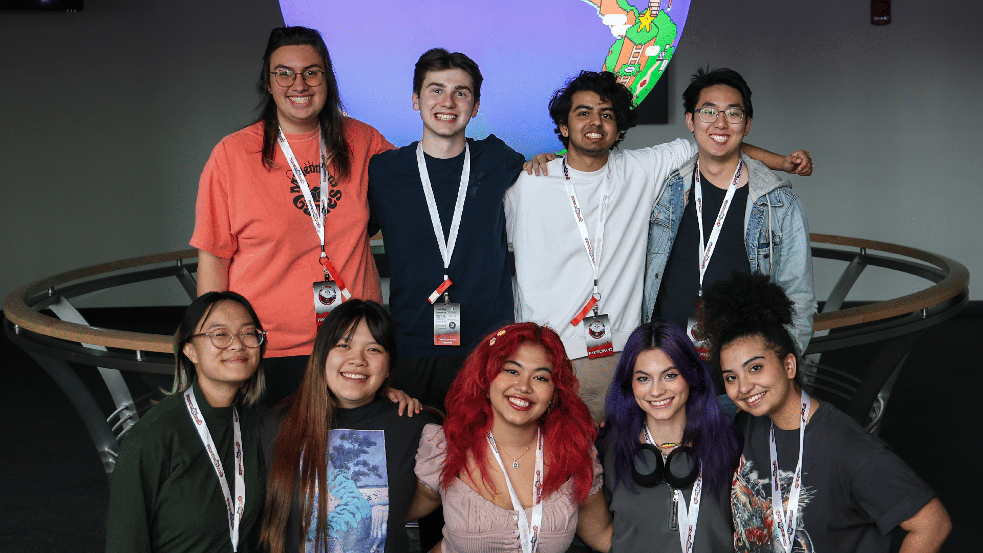 group of RIT students posing together and smiling in front of a projection of a video game