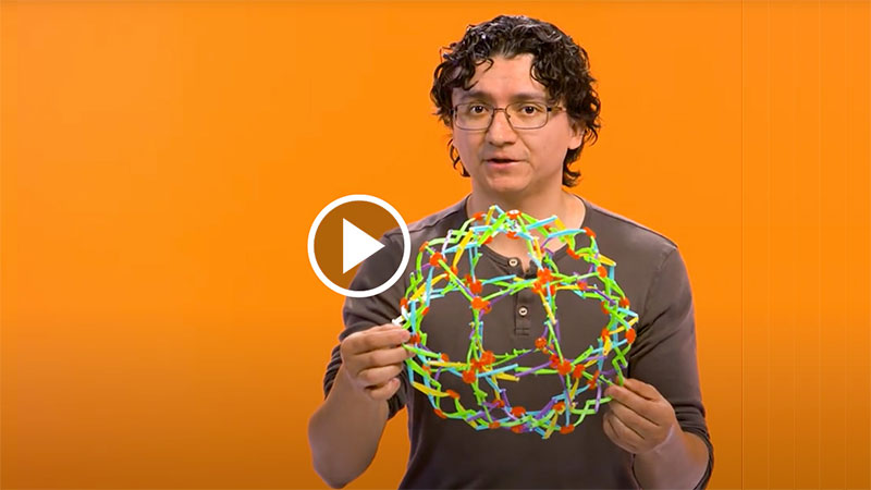 professor holding a Hoberman Sphere, a dome-like structure made of interconnected joints that can expand and contract.