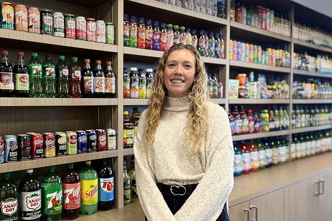 Anna Valentine, a packaging science graduate, stands in fornt of a display featuring products from Keurig Dr Pepper, inclduing bottles of Canada Dry, Squirt, and A&W soft drinks.