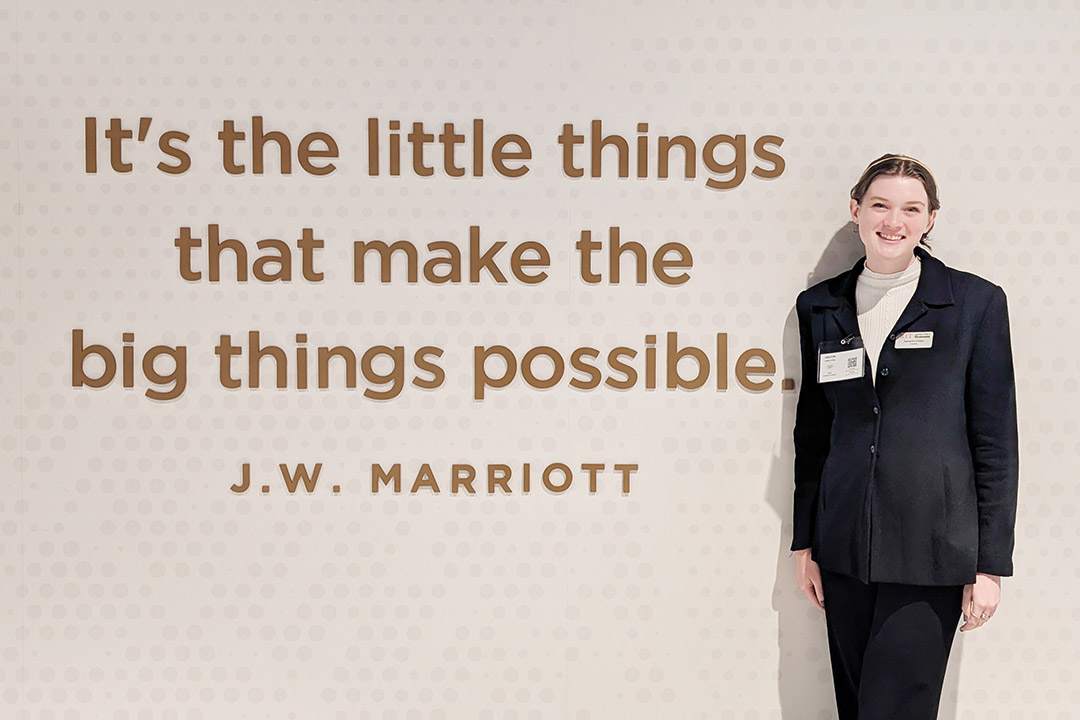 Samantha Phillips, a hospitality and tourism management major, stands in front of a sign that has a quote on from J.W. Marriott, founder of the Marriott Hotels & Resorts. The quote says, "It's the little things that make the big things possible. "
