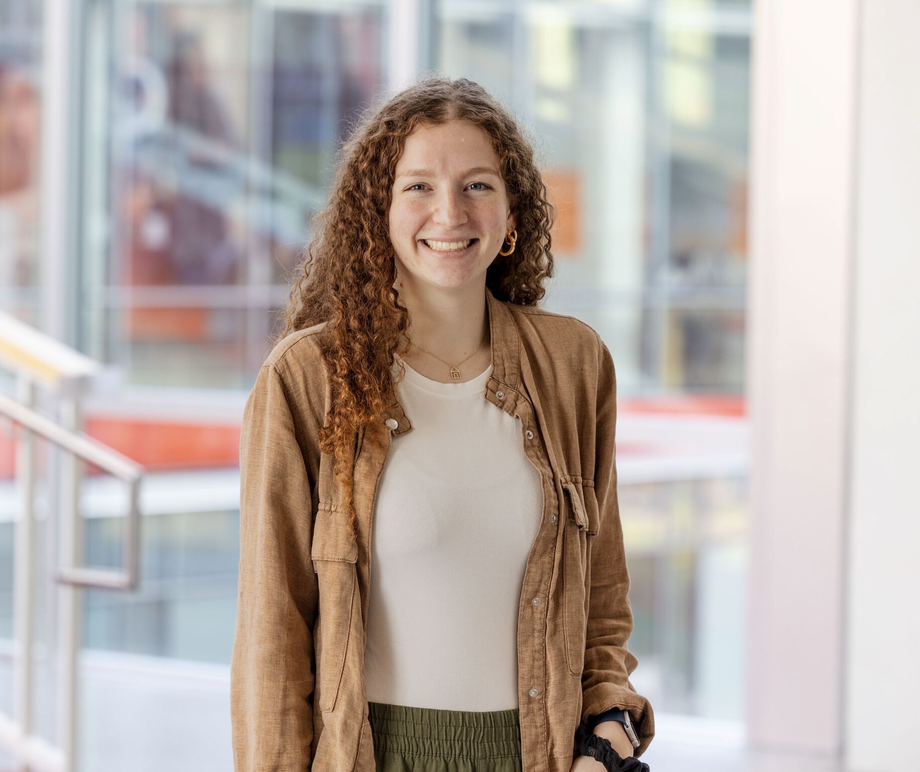 A young woman in button down shirt and green pants stands in the atrium of the RIT SHED