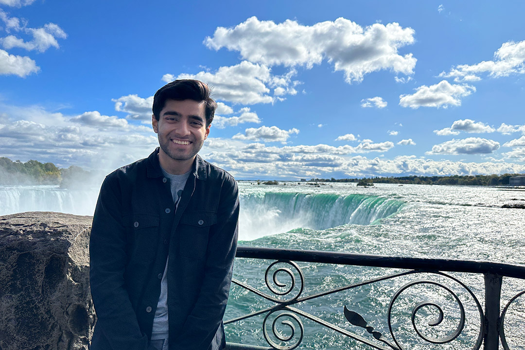 RIT student Sammy Doel wears a black jacket and stands in front of a railing overlooking Niagara Falls.