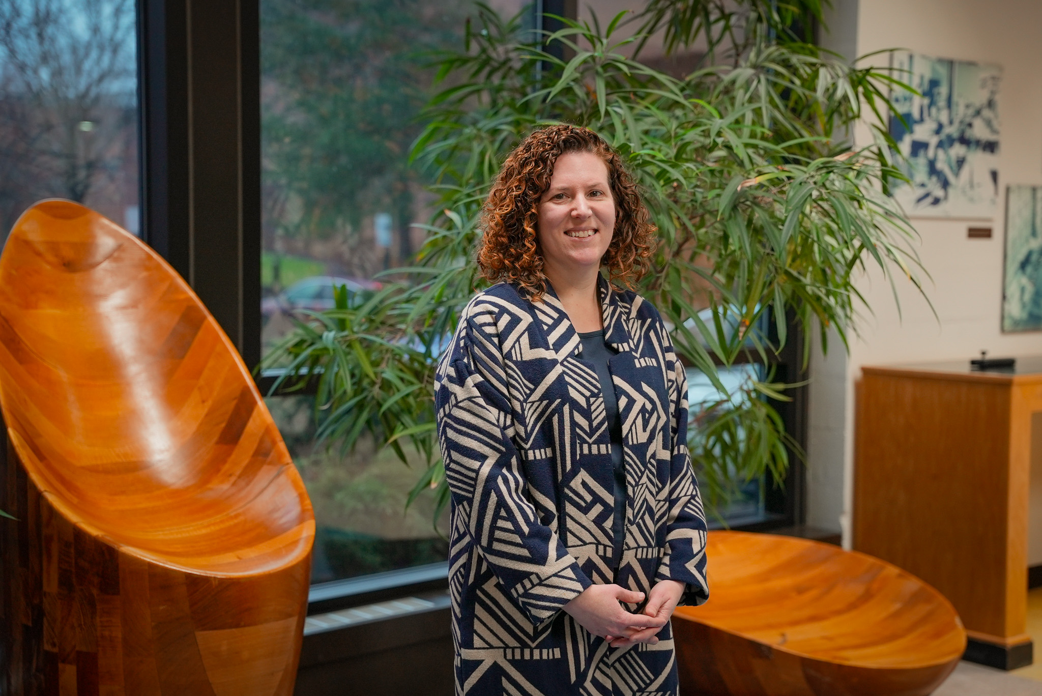 Woman standing in atrium in front of a window with a potted tree.