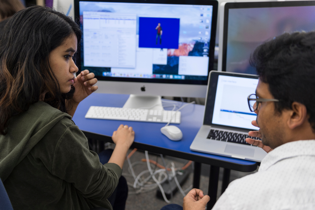 Two students talking while working on a computer