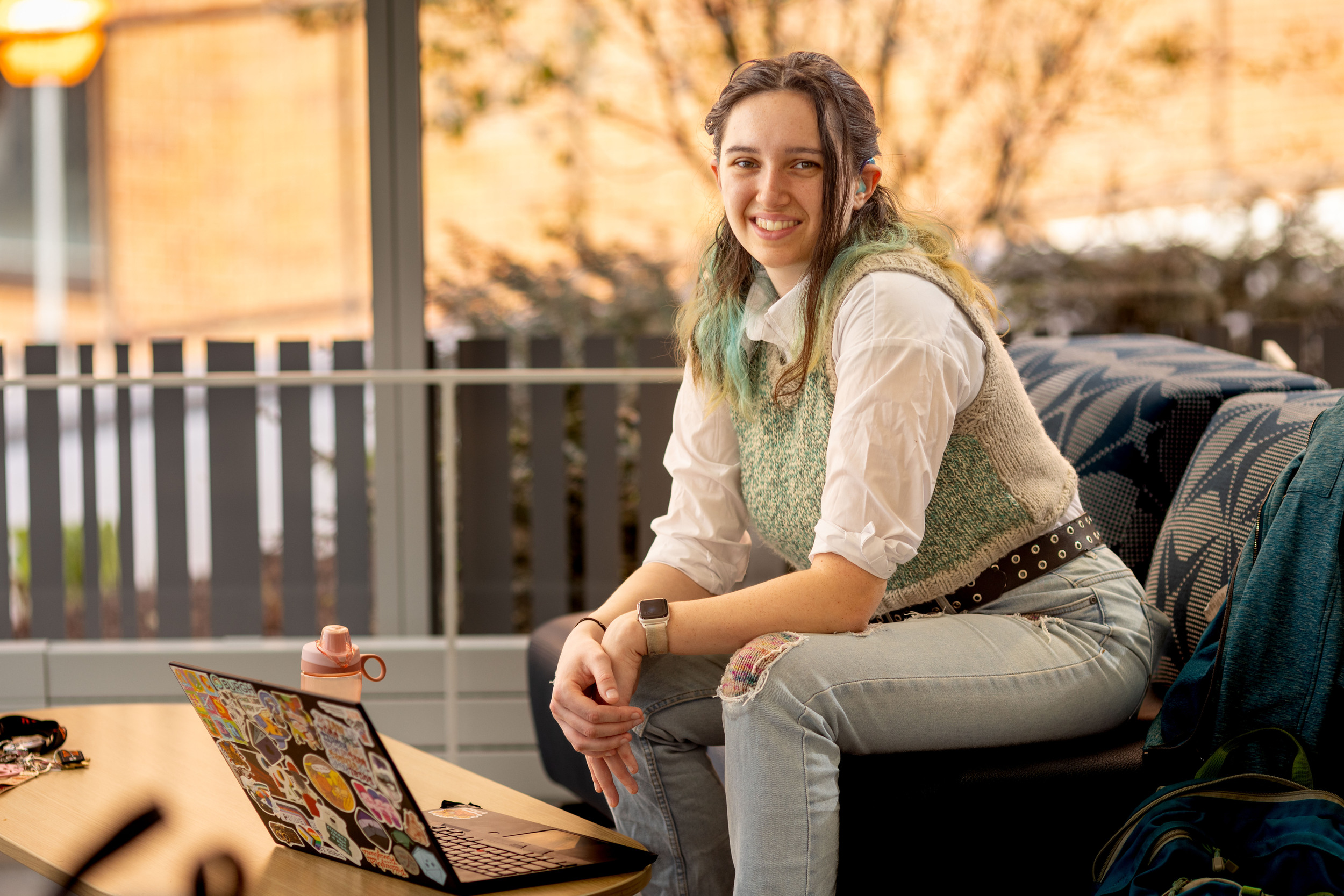 Student sits on a loveseat outside on porch