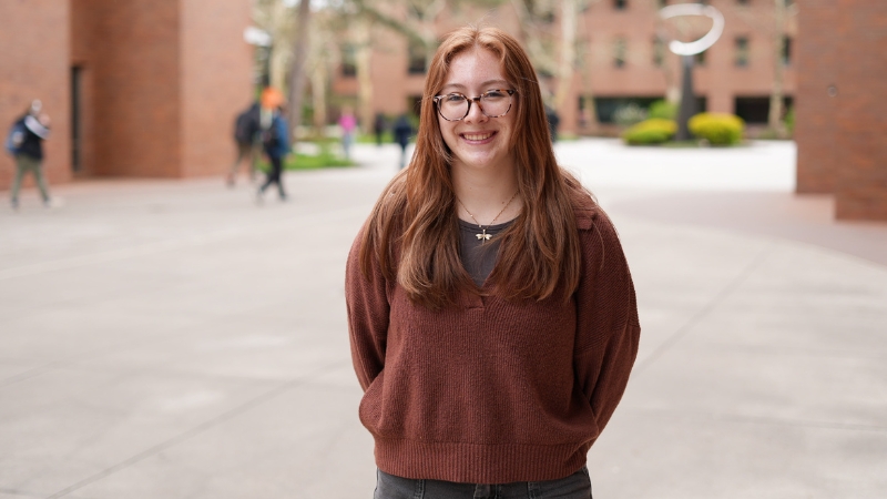 Student standing outdoors in front of brick building, smiling.