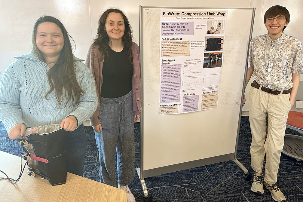 Three RIT Master's students standing on either side of a research poster and smiling.