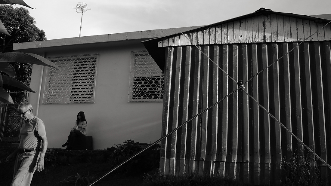 A couple people walk and stand outside a house.