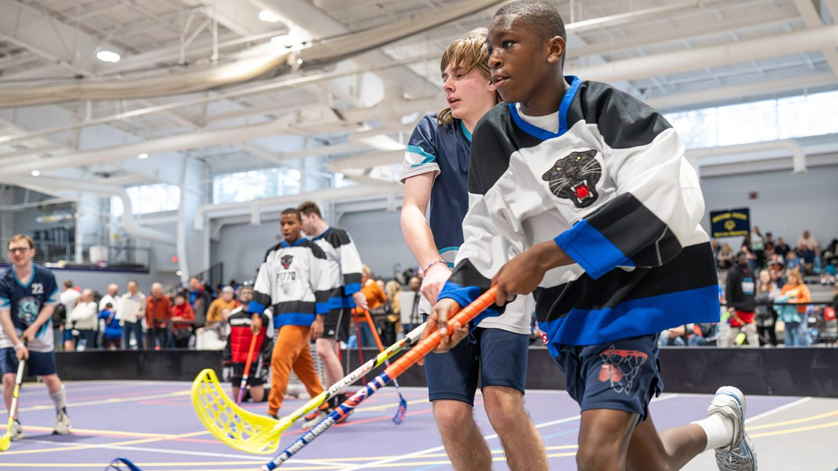 Floor hockey players run next to each other.