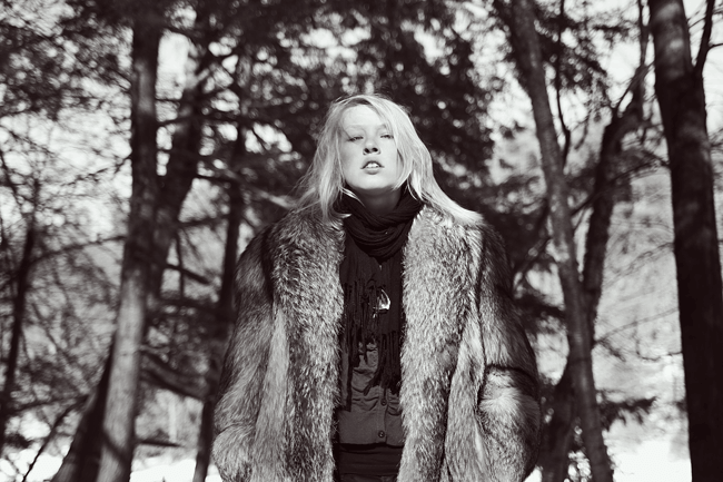 a black and white image of a woman outside wearing a fur coat.