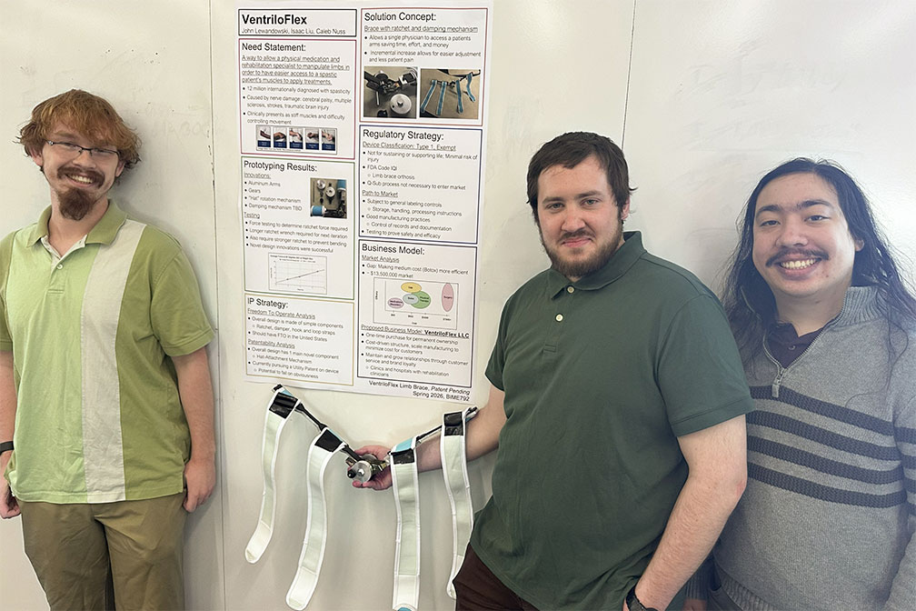Three students standing on either side of a research poster for VentriloFlex and smiling.