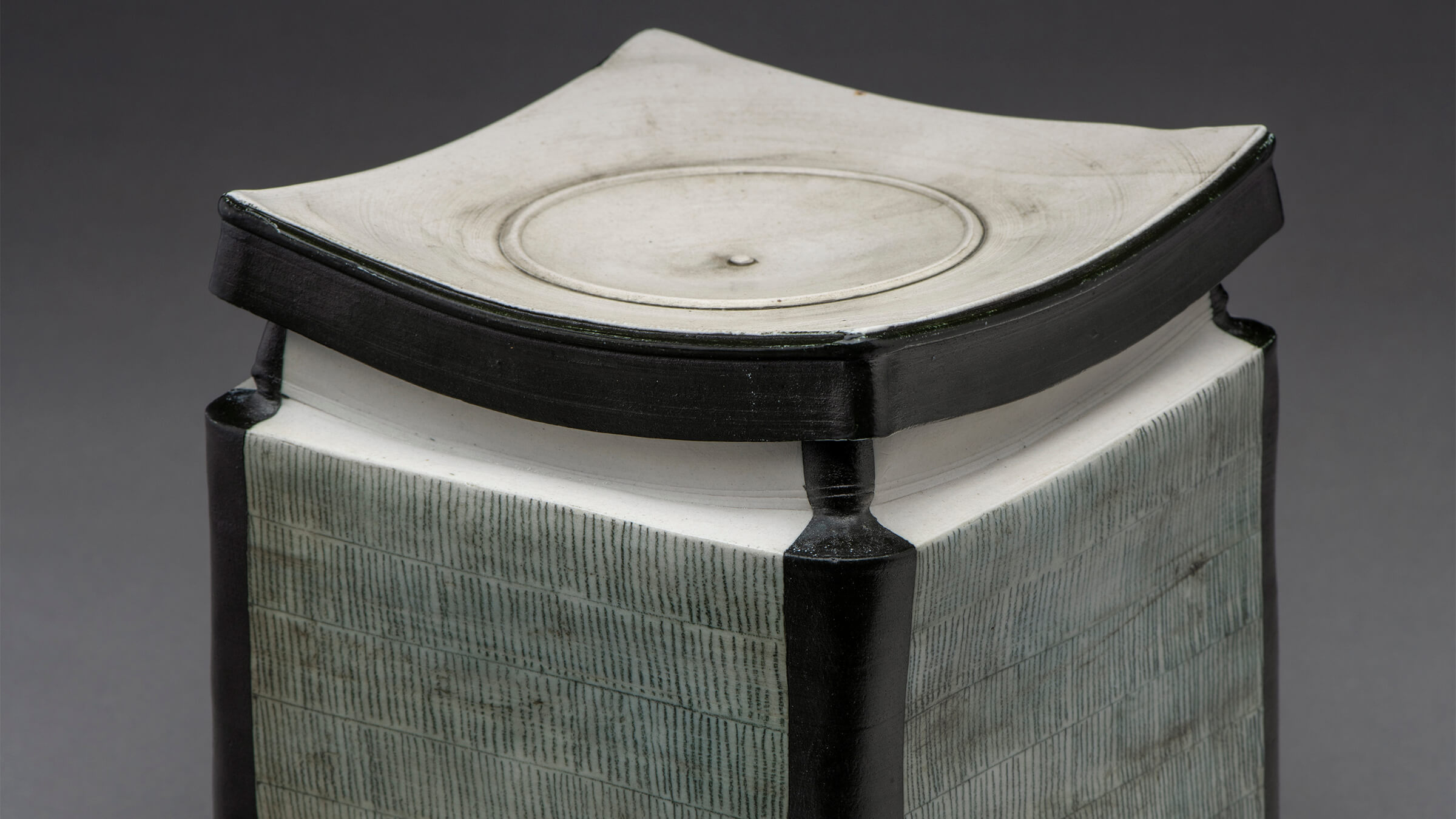 a square, porcelain box with black accents along the edges and a striation pattern along the sides.