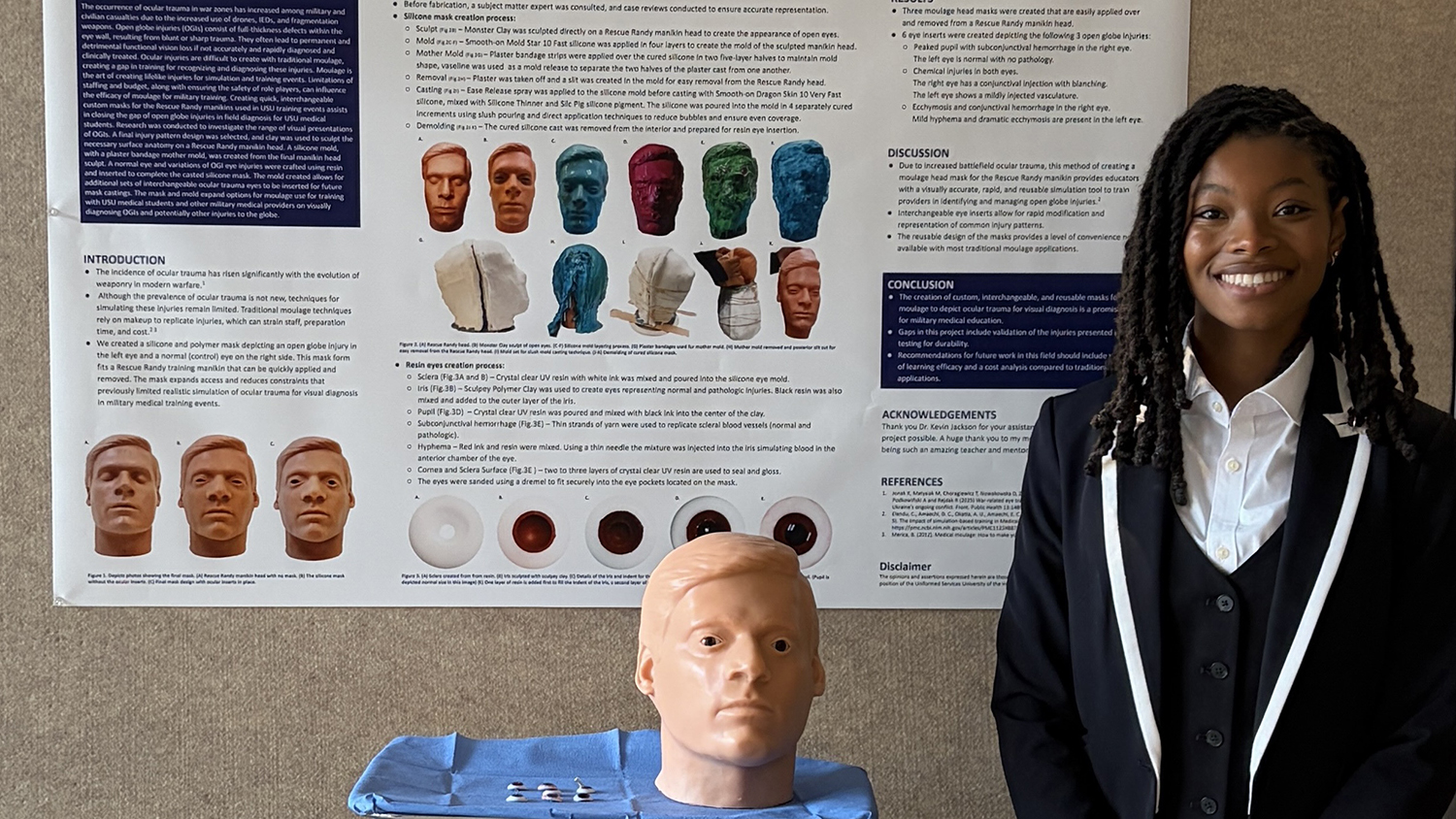 RIT medical illustration student Julia Coley stands next to a poster visualizing and describing research into using her medical illustration background to improve military health training.