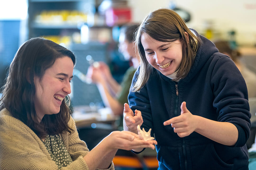 two students laugh as one holds a small shell-like object.