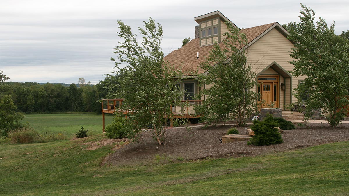 a cape-cod style home with a large deck on a large plot of land.