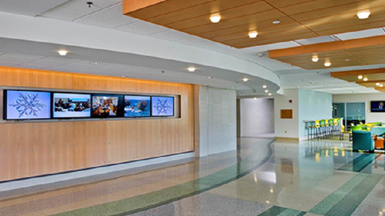a lobby with shiny floors, seating area, and T V screens showing photography.