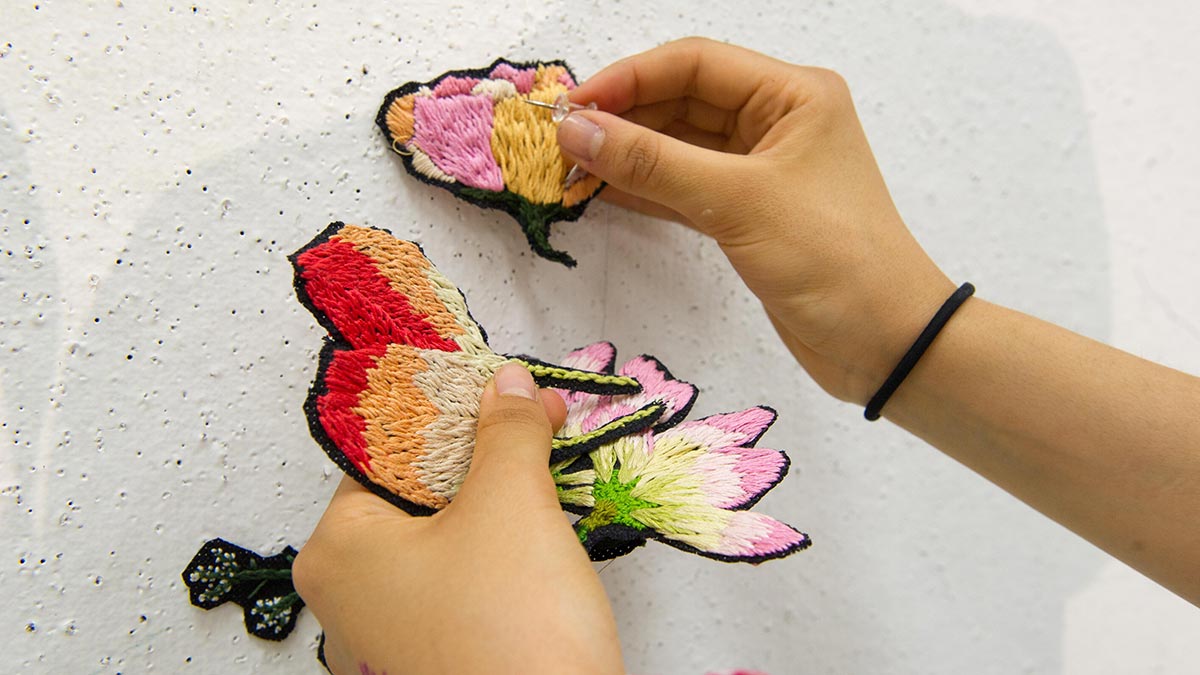 student attaches fabric flowers to wall with pushpins.
