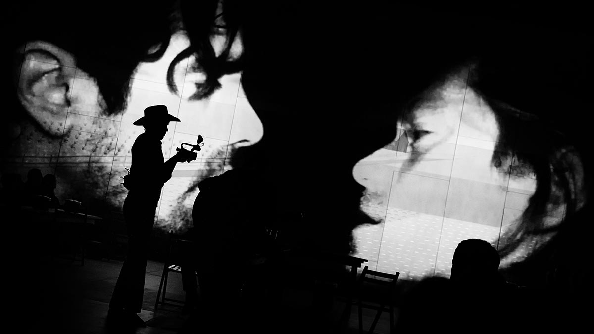 large projection of two people's faces in the background with the outline of a cowboy in the foreground.